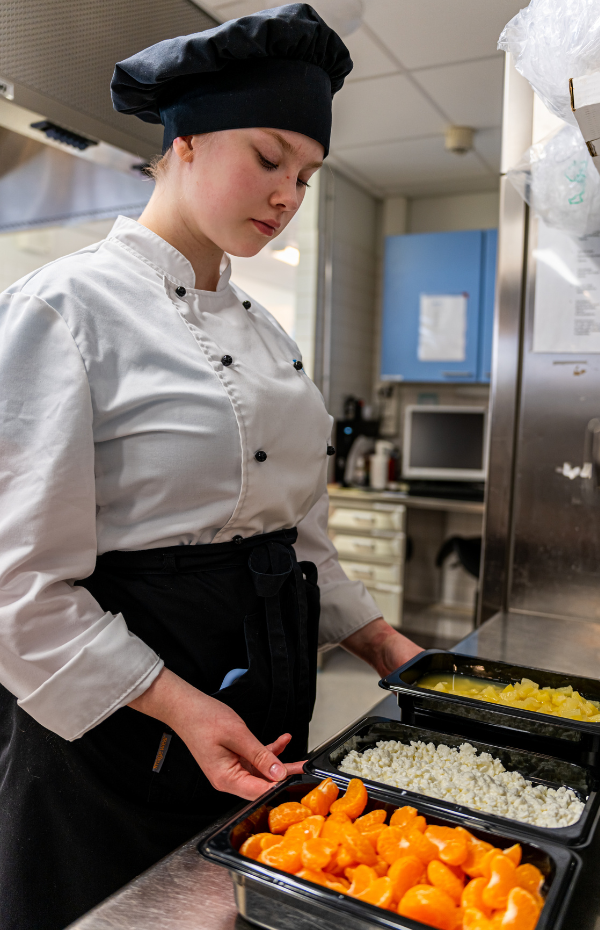 Kokkiopiskelija valmistelee tarjottavaa salaattipöytään